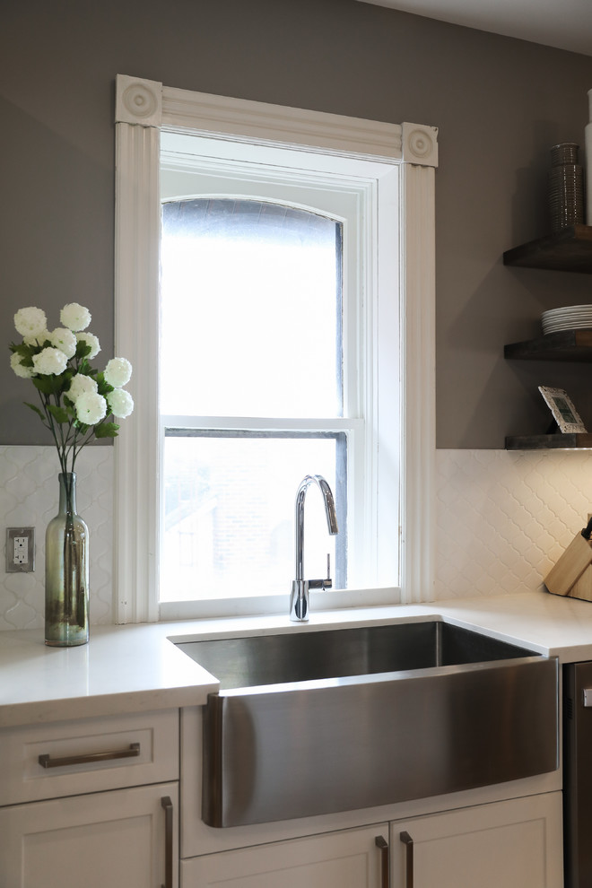 Inspiration for a mid-sized transitional single-wall medium tone wood floor and brown floor eat-in kitchen remodel with a farmhouse sink, shaker cabinets, white cabinets, white backsplash, stainless steel appliances, an island and white countertops