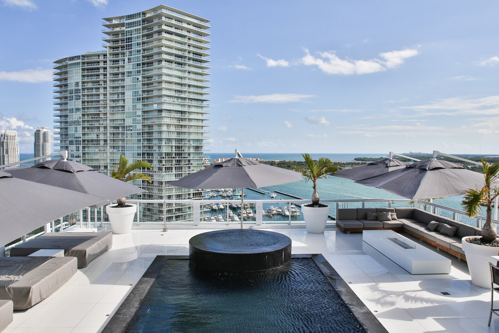 Photo of a mid-sized contemporary rooftop rectangular infinity pool in Miami with concrete slab and a hot tub.