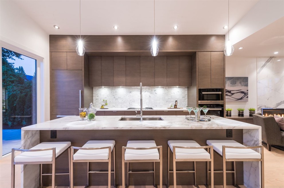 Large contemporary single-wall open plan kitchen in Vancouver with an undermount sink, flat-panel cabinets, grey cabinets, marble benchtops, white splashback, stone tile splashback, panelled appliances, light hardwood floors and with island.
