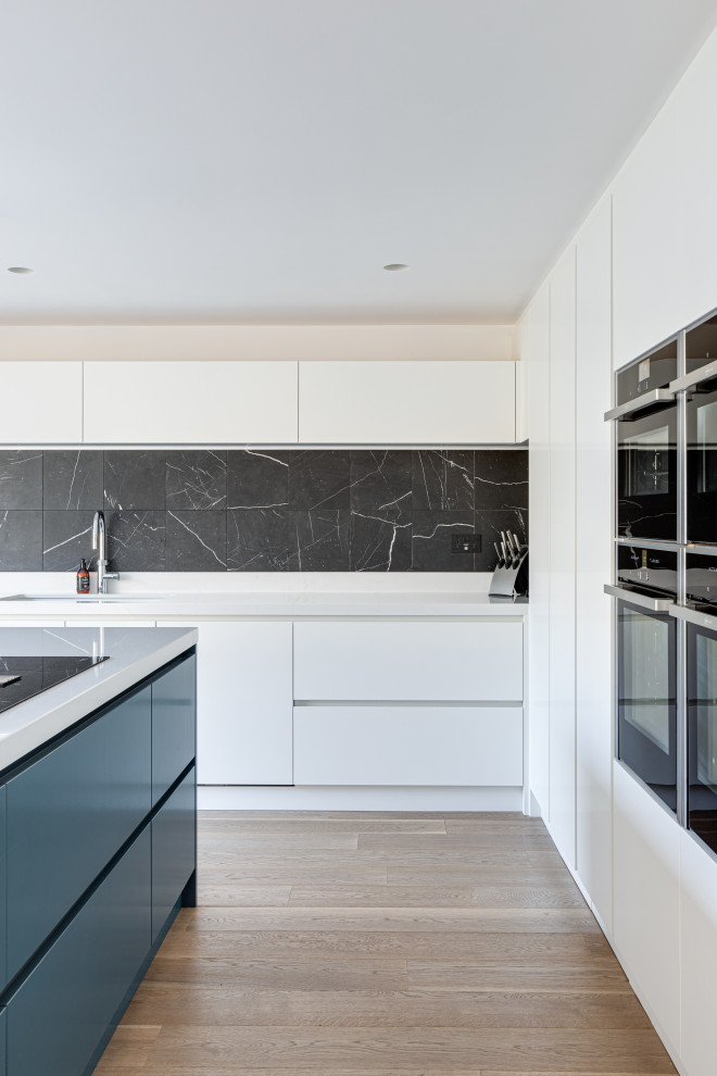 Inspiration for an expansive contemporary u-shaped eat-in kitchen in Hertfordshire with an integrated sink, flat-panel cabinets, white cabinets, quartzite benchtops, black splashback, metal splashback, black appliances, painted wood floors, with island, white floor and white benchtop.