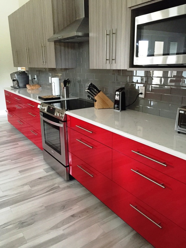 This is an example of a large eclectic single-wall open plan kitchen in Jacksonville with an undermount sink, flat-panel cabinets, red cabinets, quartz benchtops, grey splashback, glass tile splashback, stainless steel appliances, porcelain floors and with island.