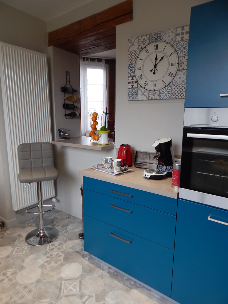 This is an example of a mid-sized contemporary galley open plan kitchen in Le Havre with an undermount sink, flat-panel cabinets, blue cabinets, laminate benchtops, beige splashback, black appliances, cement tiles, no island and beige floor.
