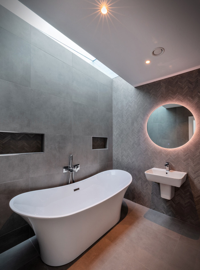 На фото: главная ванная комната среднего размера в современном стиле с отдельно стоящей ванной, серой плиткой, каменной плиткой, серыми стенами, полом из керамической плитки, подвесной раковиной, серым полом, нишей и тумбой под одну раковину с