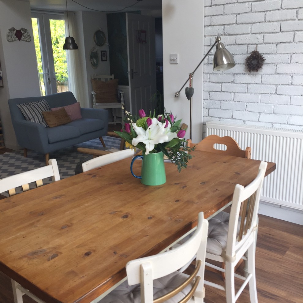 This is an example of a mid-sized country open plan dining in Sussex with white walls, laminate floors, a wood stove and a tile fireplace surround.