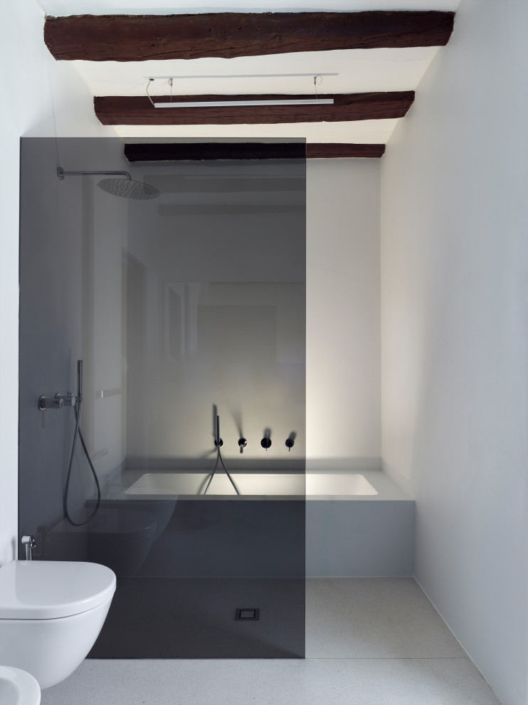 Modelo de cuarto de baño contemporáneo grande sin sin inodoro con bañera encastrada, sanitario de pared, paredes blancas, suelo de terrazo, suelo gris y vigas vistas