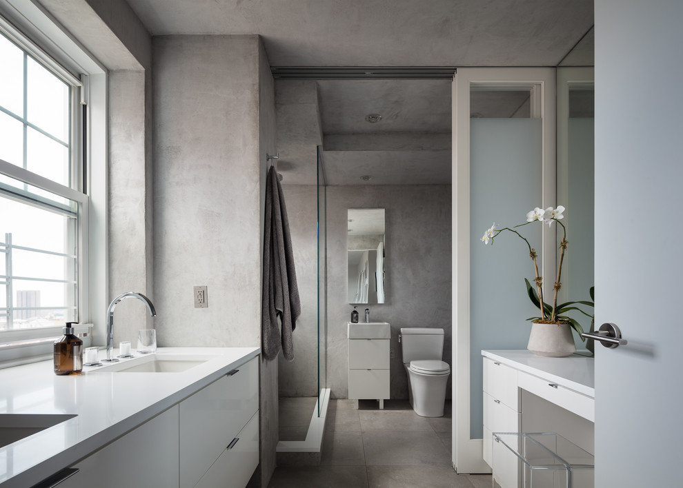 Photo of a contemporary master bathroom in New York with flat-panel cabinets, white cabinets, an alcove shower, a two-piece toilet, grey walls, an undermount sink, grey floor, an open shower and white benchtops.