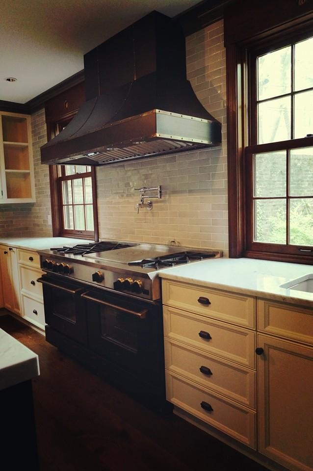 Inspiration for a transitional l-shaped kitchen in Cleveland with recessed-panel cabinets, white cabinets, with island, a farmhouse sink, marble benchtops, porcelain splashback, stainless steel appliances and dark hardwood floors.