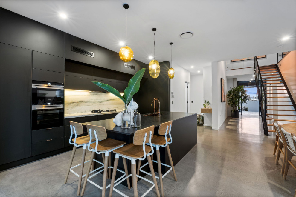 Inspiration for a contemporary galley kitchen in Sunshine Coast with an undermount sink, flat-panel cabinets, black cabinets, white splashback, stone slab splashback, black appliances, concrete floors, with island, grey floor and white benchtop.
