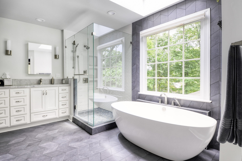 Photo of a mid-sized modern master bathroom in DC Metro with recessed-panel cabinets, white cabinets, a freestanding tub, a corner shower, a two-piece toilet, white tile, ceramic tile, grey walls, cement tiles, an undermount sink, marble benchtops, grey floor, a hinged shower door and white benchtops.