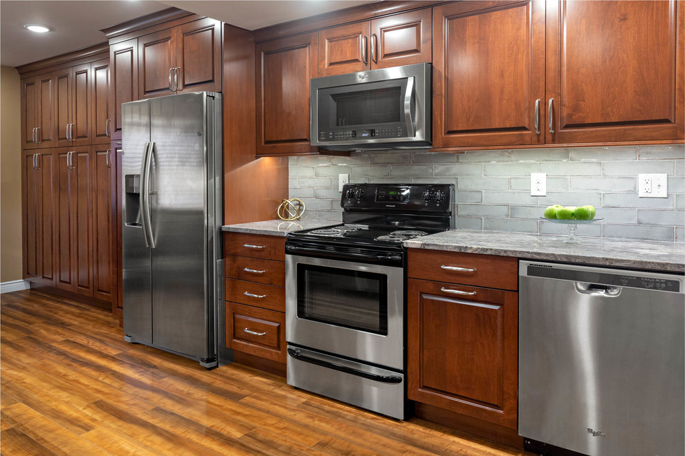 Inspiration for a mid-sized transitional light wood floor eat-in kitchen remodel with a single-bowl sink, recessed-panel cabinets, dark wood cabinets, granite countertops, gray backsplash, subway tile backsplash, stainless steel appliances and gray countertops