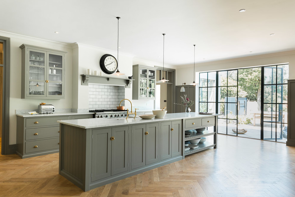 Photo of a transitional kitchen in London with glass-front cabinets, grey cabinets, white splashback, subway tile splashback, stainless steel appliances, medium hardwood floors and with island.