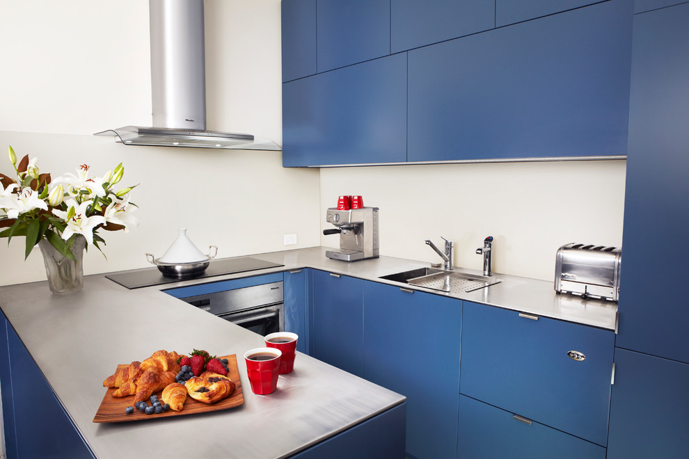 This is an example of a small contemporary u-shaped eat-in kitchen in Sydney with an integrated sink, flat-panel cabinets, blue cabinets, stainless steel benchtops, white splashback, stainless steel appliances and porcelain floors.