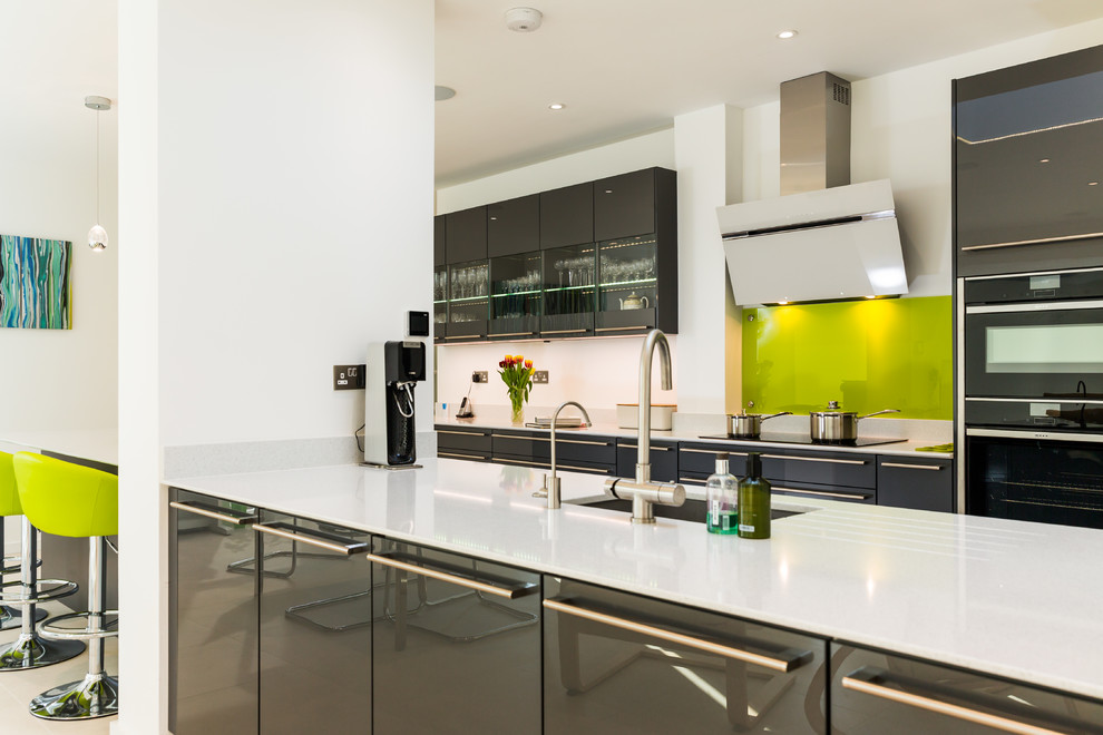 Photo of a large contemporary galley eat-in kitchen in Hampshire with flat-panel cabinets, grey cabinets, quartzite benchtops, green splashback, glass sheet splashback, porcelain floors, multiple islands, an integrated sink and panelled appliances.