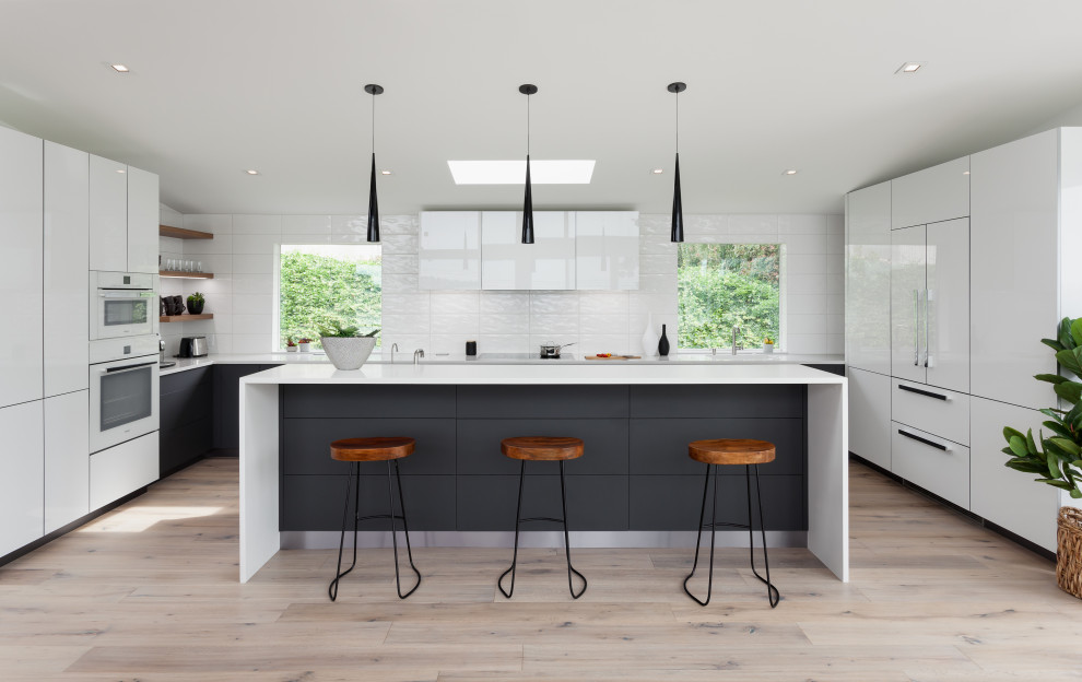 Inspiration for a contemporary u-shaped open plan kitchen in Seattle with flat-panel cabinets, white cabinets, white splashback, panelled appliances, light hardwood floors, with island, beige floor and white benchtop.