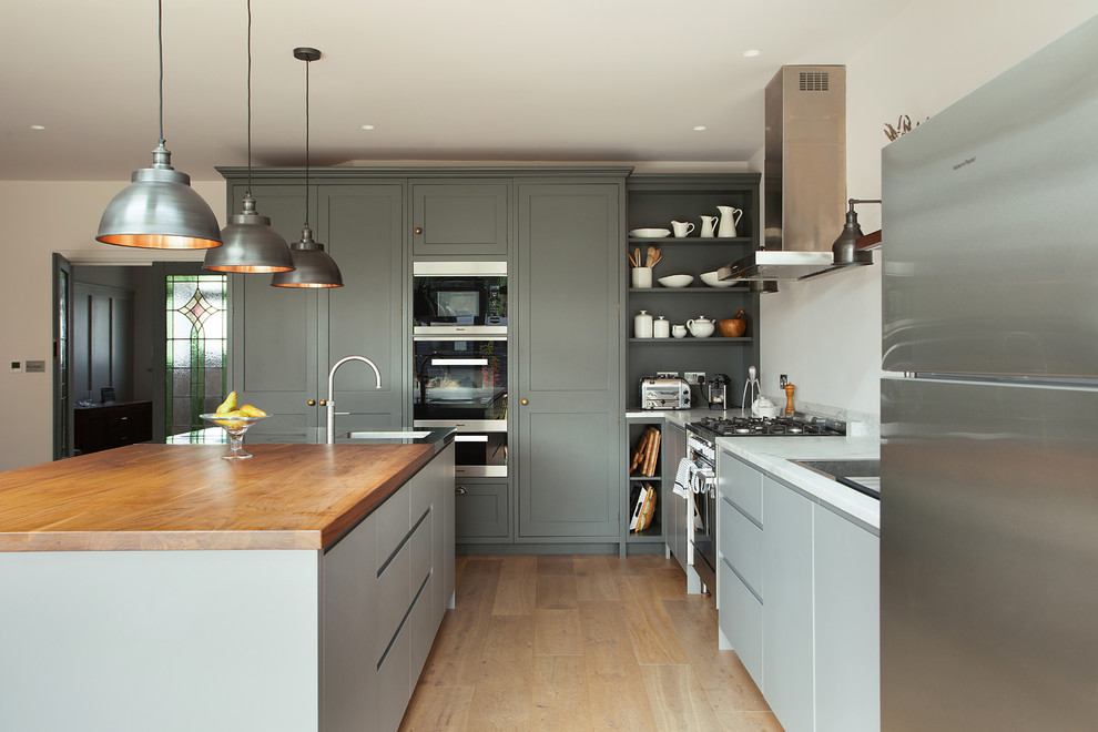 Design ideas for a transitional l-shaped eat-in kitchen in London with an integrated sink, shaker cabinets, grey cabinets, wood benchtops, stainless steel appliances, light hardwood floors, with island, beige floor and brown benchtop.