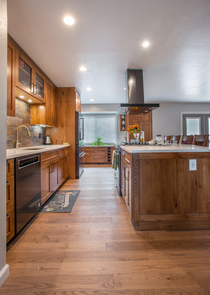 Large country l-shaped eat-in kitchen in Other with an undermount sink, shaker cabinets, brown cabinets, quartz benchtops, multi-coloured splashback, slate splashback, stainless steel appliances, medium hardwood floors, with island, brown floor and white benchtop.