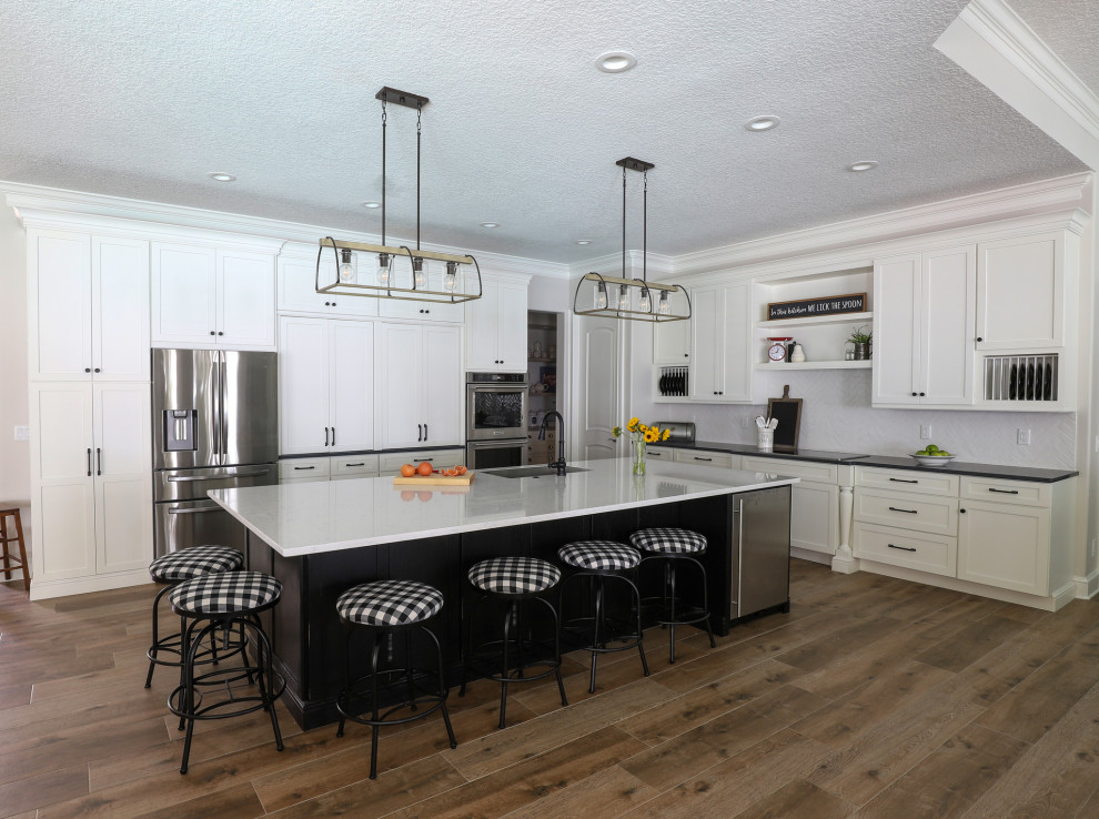 Photo of a large country l-shaped open plan kitchen in Jacksonville with an undermount sink, shaker cabinets, black cabinets, quartz benchtops, white splashback, ceramic splashback, stainless steel appliances, porcelain floors, with island, brown floor and black benchtop.