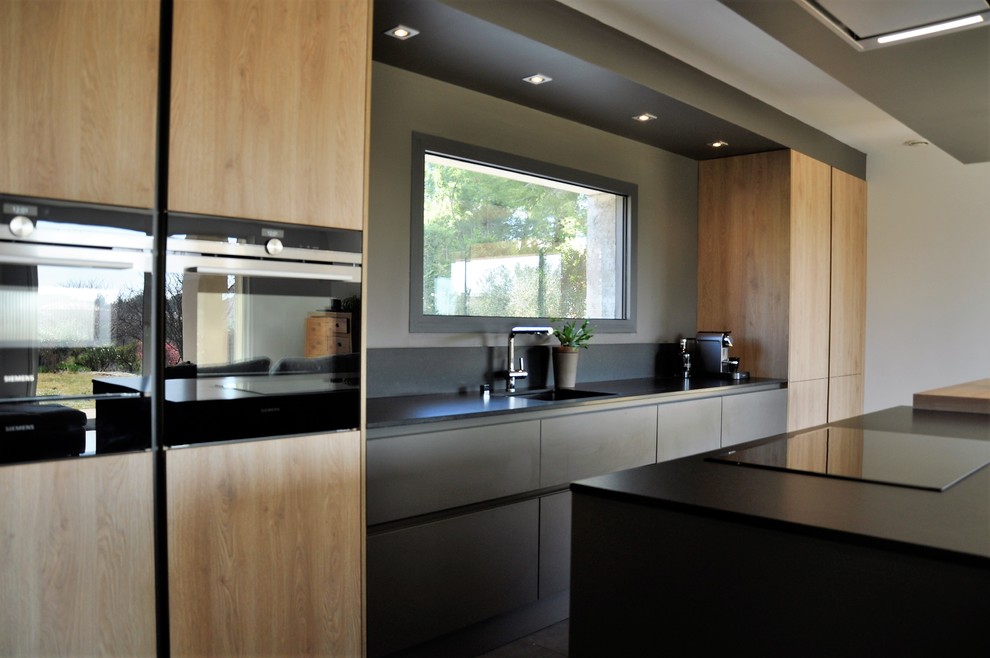 Inspiration for a contemporary galley kitchen in Marseille with granite benchtops, black splashback, black appliances, ceramic floors, with island, grey floor and black benchtop.