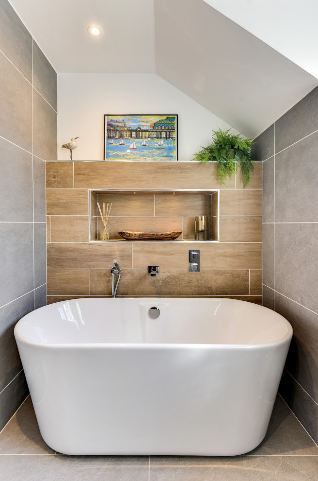 Photo of a large modern grey and white ensuite bathroom in Sussex with flat-panel cabinets, grey cabinets, a freestanding bath, a walk-in shower, a one-piece toilet, grey tiles, ceramic tiles, grey walls, ceramic flooring, a built-in sink, glass worktops, grey floors, an open shower, white worktops, feature lighting, a single sink and a floating vanity unit.