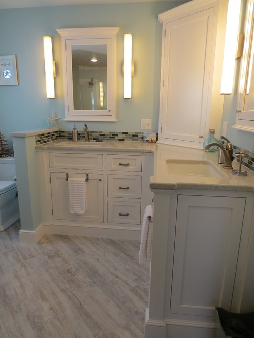 The soft blue and greens of this bathroom compliment the white vanity, which has a tall medicine cabinet in the center of the L-shape.