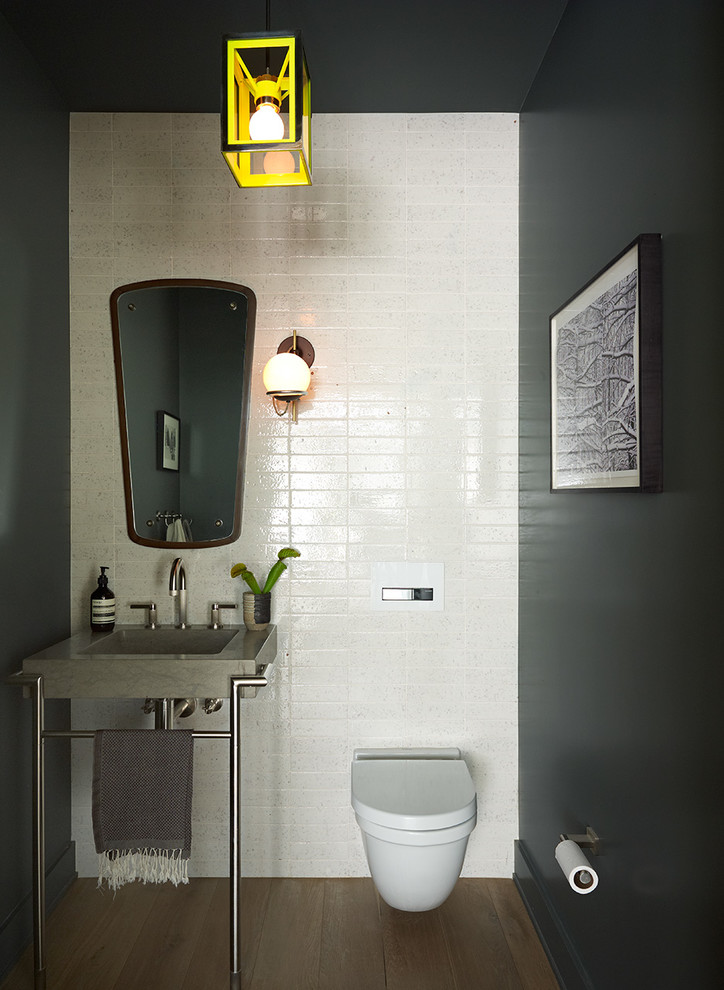 This is an example of a small contemporary powder room in New York with a pedestal sink, a wall-mount toilet, black walls and medium hardwood floors.