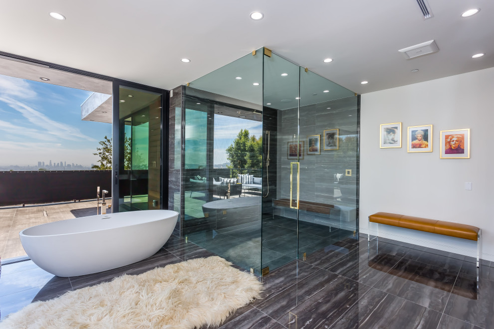 Modern inredning av ett stort en-suite badrum, med ett fristående badkar, en hörndusch, svart kakel, kakelplattor, grå väggar, kalkstensgolv, svart golv och dusch med gångjärnsdörr
