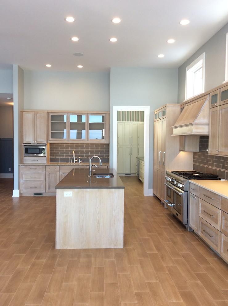 Large arts and crafts single-wall open plan kitchen in Grand Rapids with an undermount sink, shaker cabinets, medium wood cabinets, solid surface benchtops, brown splashback, subway tile splashback, panelled appliances, laminate floors, with island and brown floor.