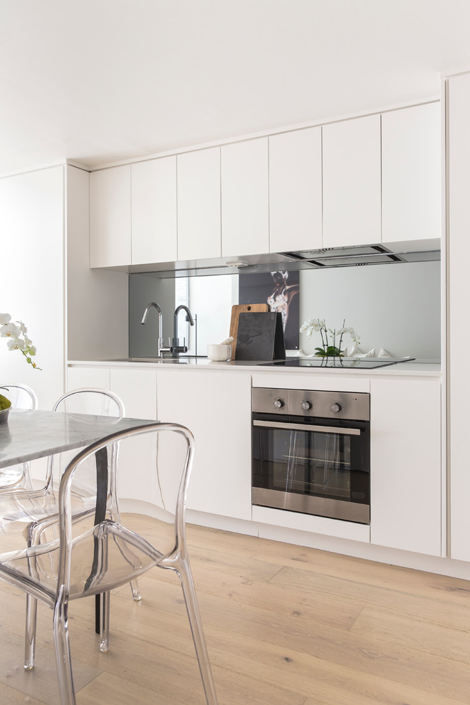 Photo of a small contemporary single-wall eat-in kitchen in Sydney with an integrated sink, white cabinets, quartz benchtops, metallic splashback, mirror splashback, stainless steel appliances, light hardwood floors and no island.