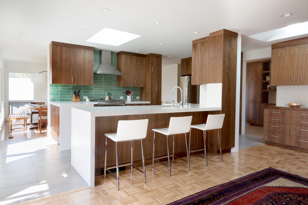 Design ideas for a mid-sized midcentury l-shaped kitchen in San Francisco with an undermount sink, flat-panel cabinets, dark wood cabinets, solid surface benchtops, green splashback, ceramic splashback, stainless steel appliances, porcelain floors and a peninsula.