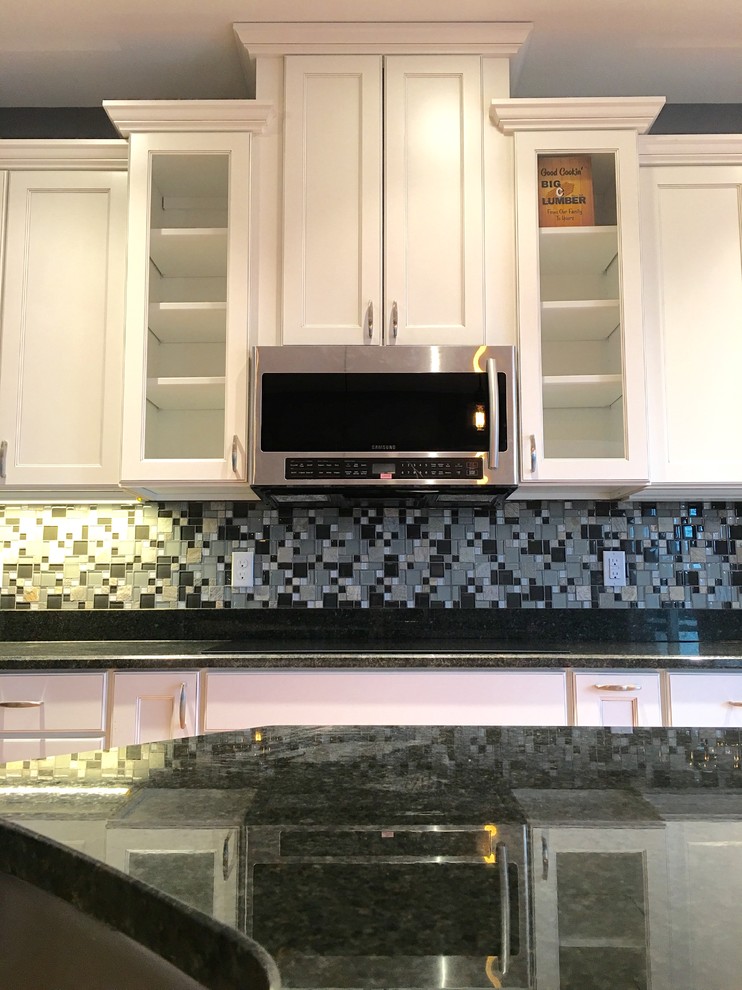 Inspiration for a large transitional l-shaped light wood floor eat-in kitchen remodel with an undermount sink, recessed-panel cabinets, white cabinets, granite countertops, multicolored backsplash, glass tile backsplash, stainless steel appliances and an island