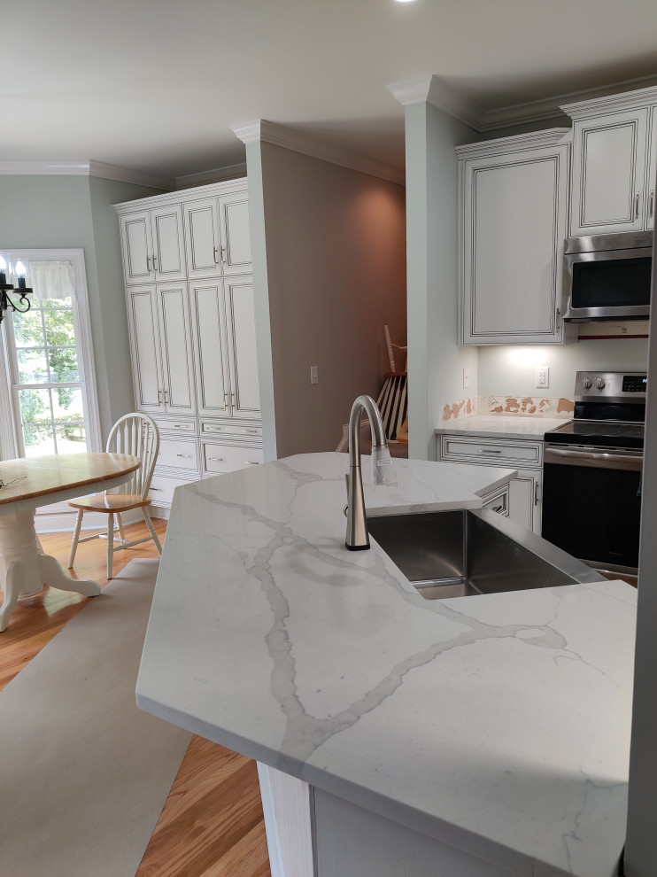 Kitchen - mid-sized medium tone wood floor kitchen idea in Charlotte with a single-bowl sink, shaker cabinets, white cabinets, quartzite countertops, gray backsplash, glass tile backsplash, stainless steel appliances and white countertops