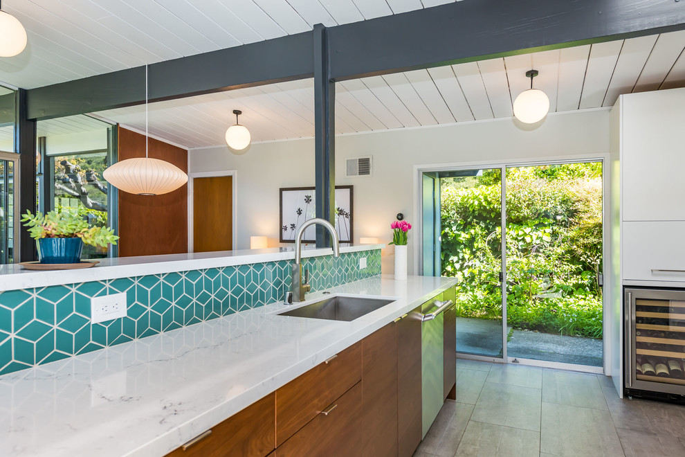 This is an example of a mid-sized midcentury single-wall open plan kitchen in San Francisco with a drop-in sink, flat-panel cabinets, white cabinets, quartzite benchtops, blue splashback, ceramic splashback, stainless steel appliances, painted wood floors, a peninsula, grey floor and white benchtop.