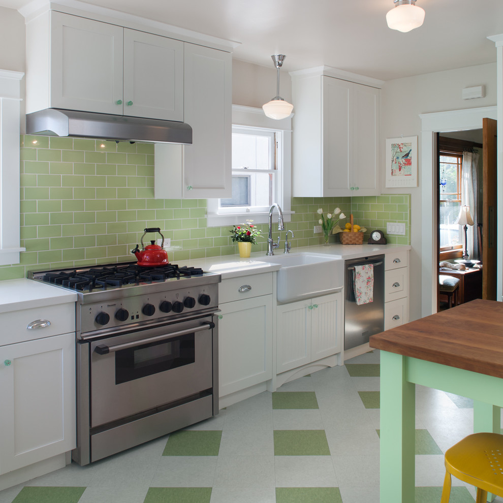 Design ideas for a mid-sized traditional l-shaped eat-in kitchen in San Diego with a farmhouse sink, shaker cabinets, white cabinets, solid surface benchtops, green splashback, subway tile splashback, stainless steel appliances, linoleum floors, green floor and white benchtop.