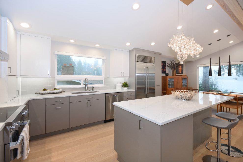 Design ideas for a large contemporary l-shaped eat-in kitchen in Seattle with an undermount sink, flat-panel cabinets, grey cabinets, grey splashback, glass tile splashback, stainless steel appliances, with island, beige floor and white benchtop.