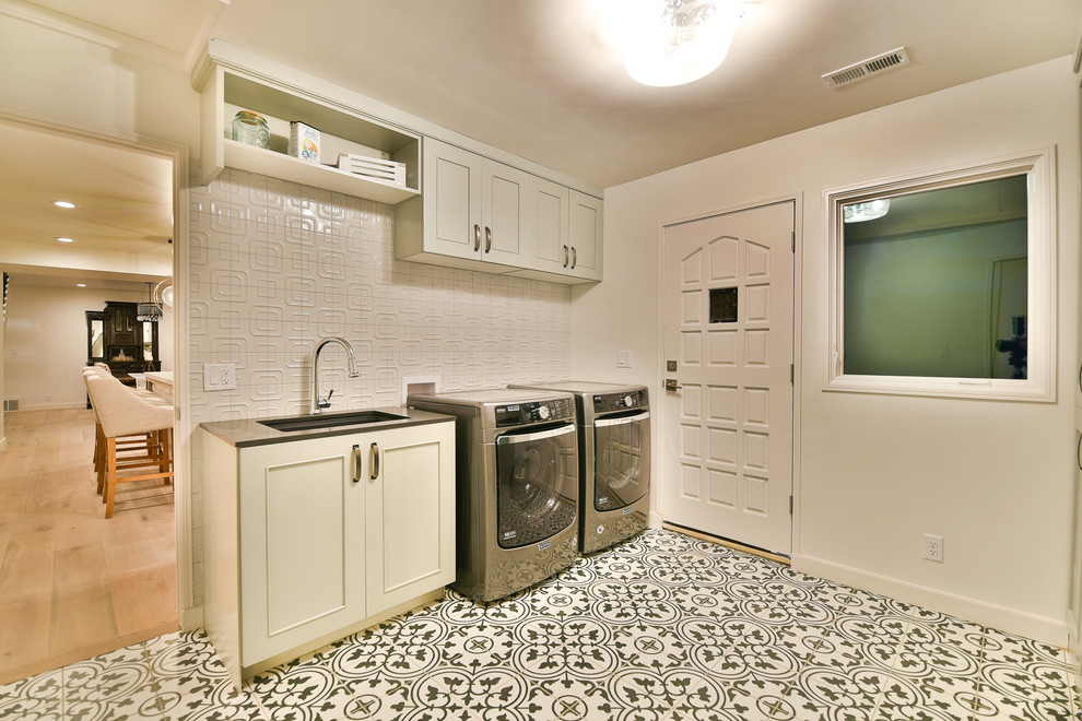 This is an example of a mid-sized transitional galley utility room in Salt Lake City with an undermount sink, shaker cabinets, grey cabinets, solid surface benchtops, white walls, ceramic floors, a side-by-side washer and dryer and multi-coloured floor.
