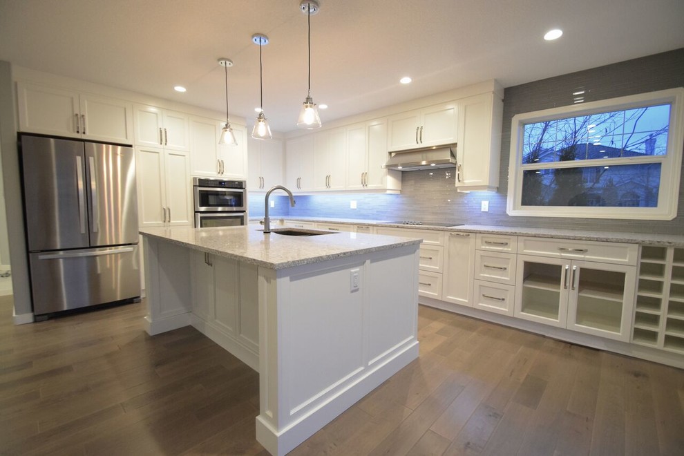 Inspiration for a transitional l-shaped vinyl floor eat-in kitchen remodel in Edmonton with a double-bowl sink, shaker cabinets, white cabinets, quartz countertops, gray backsplash, glass tile backsplash, stainless steel appliances and an island