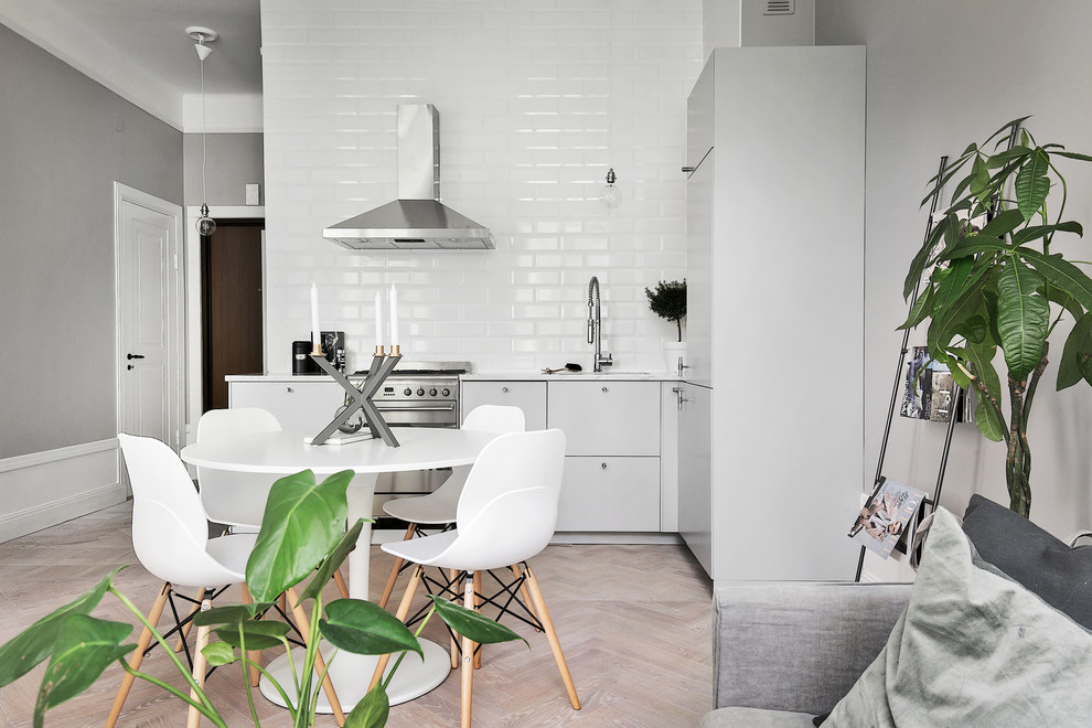 Design ideas for a mid-sized scandinavian l-shaped eat-in kitchen in Stockholm with an undermount sink, flat-panel cabinets, grey cabinets, white splashback, subway tile splashback, stainless steel appliances, light hardwood floors and no island.