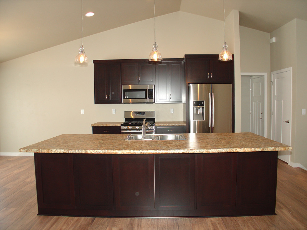 Example of a mid-sized l-shaped light wood floor, brown floor and vaulted ceiling open concept kitchen design with recessed-panel cabinets, laminate countertops, an island and a drop-in sink