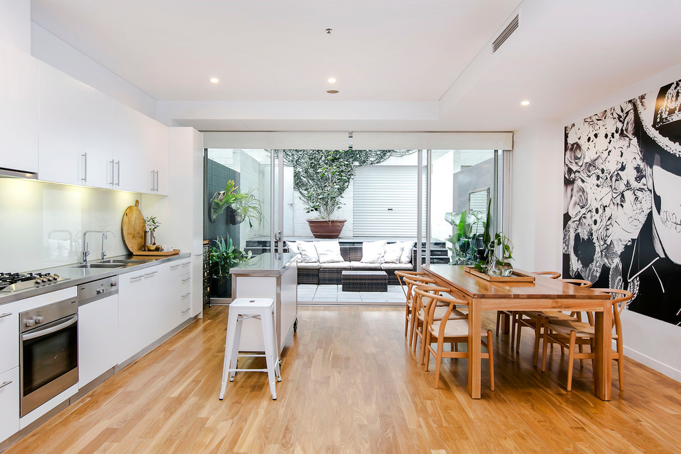 Inspiration for a large scandinavian single-wall eat-in kitchen in Adelaide with a double-bowl sink, flat-panel cabinets, white cabinets, stainless steel benchtops, white splashback, medium hardwood floors and with island.