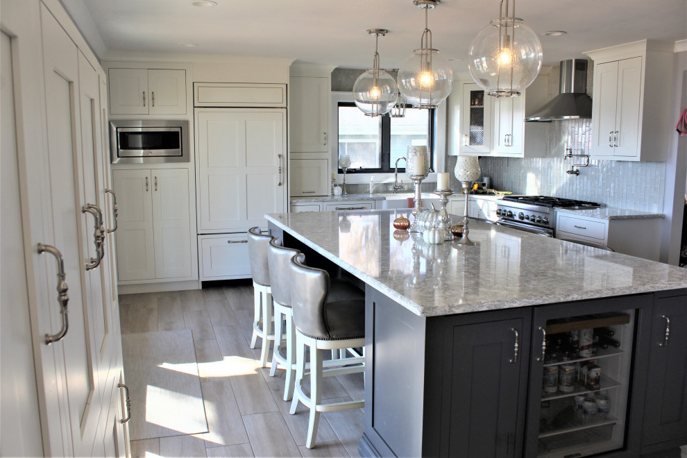This is an example of a large transitional l-shaped open plan kitchen in Detroit with a farmhouse sink, recessed-panel cabinets, white cabinets, quartz benchtops, white splashback, ceramic splashback, panelled appliances, medium hardwood floors, with island, brown floor and multi-coloured benchtop.