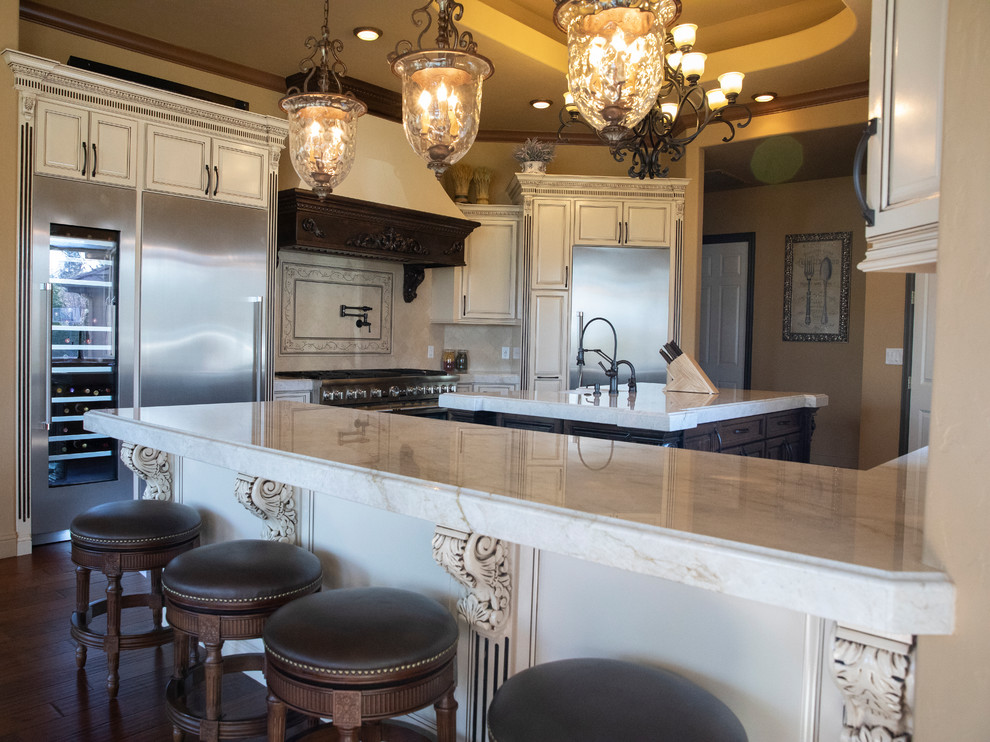 Large tuscan l-shaped dark wood floor and brown floor eat-in kitchen photo with a farmhouse sink, raised-panel cabinets, distressed cabinets, quartz countertops, beige backsplash, stone tile backsplash, stainless steel appliances, an island and multicolored countertops