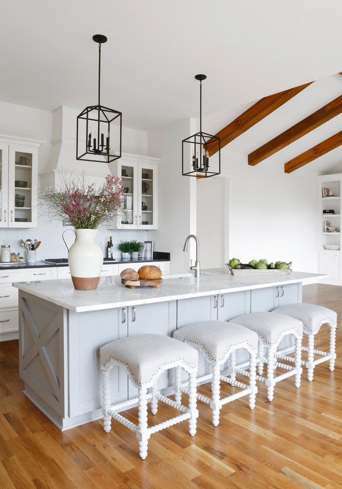 Inspiration for a mid-sized country l-shaped open plan kitchen in Nashville with shaker cabinets, white cabinets, marble benchtops, white splashback, subway tile splashback, stainless steel appliances, with island, white benchtop, a farmhouse sink, medium hardwood floors and brown floor.