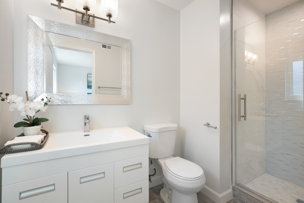 Foto på ett litet funkis vit badrum med dusch, med släta luckor, vita skåp, en dusch i en alkov, en toalettstol med separat cisternkåpa, flerfärgad kakel, porslinskakel, grå väggar, klinkergolv i porslin, ett integrerad handfat, bänkskiva i akrylsten, grått golv och dusch med gångjärnsdörr