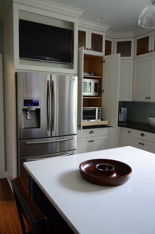 Inspiration for a mid-sized transitional l-shaped dark wood floor eat-in kitchen remodel with a single-bowl sink, shaker cabinets, white cabinets, solid surface countertops, white backsplash, glass tile backsplash, stainless steel appliances and an island