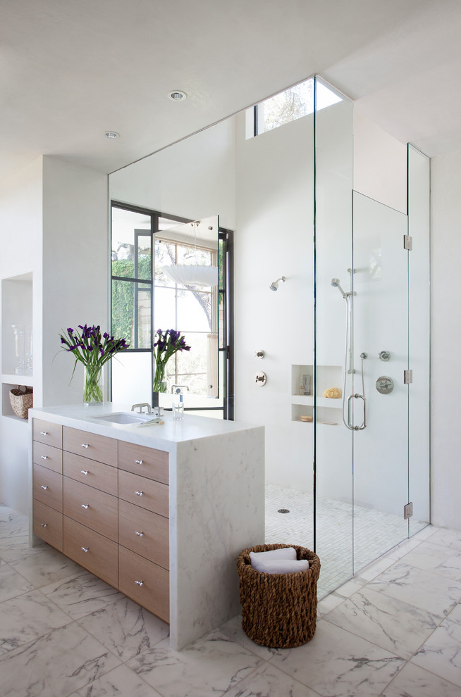 This is an example of a large mediterranean master bathroom in Austin with flat-panel cabinets, medium wood cabinets, a curbless shower, white tile, white walls and marble floors.