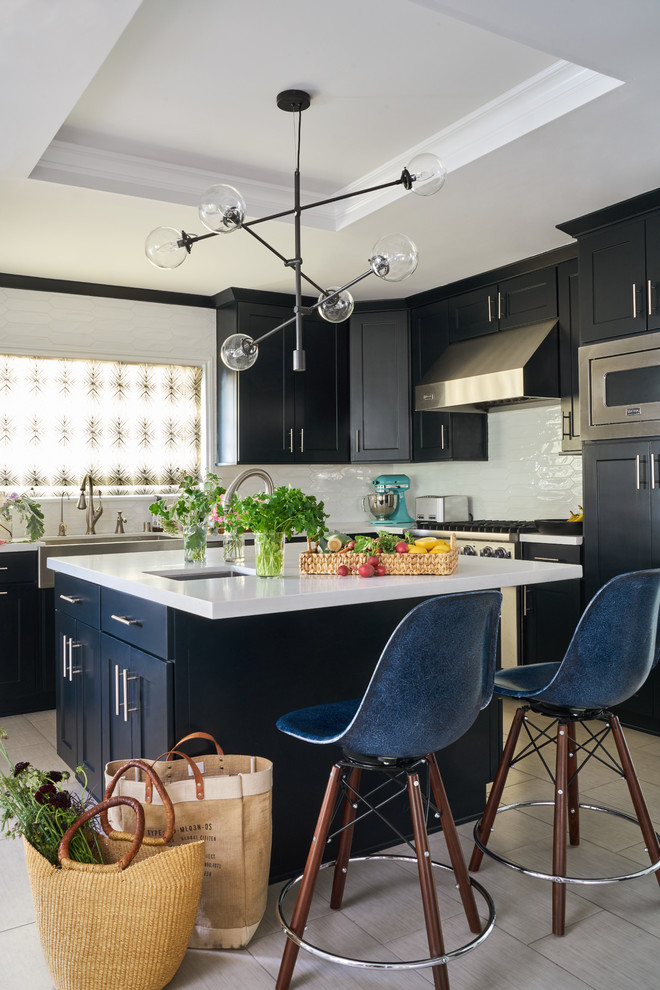 Design ideas for a mid-sized transitional l-shaped open plan kitchen in Charlotte with a farmhouse sink, shaker cabinets, black cabinets, white splashback, stainless steel appliances, with island, white benchtop, quartz benchtops, porcelain floors and beige floor.