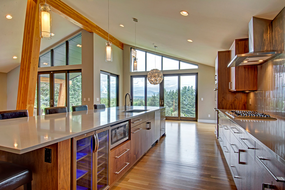 Large contemporary galley kitchen pantry in Denver with flat-panel cabinets, medium wood cabinets, granite benchtops, beige splashback, light hardwood floors, with island, an undermount sink, ceramic splashback, stainless steel appliances and brown floor.