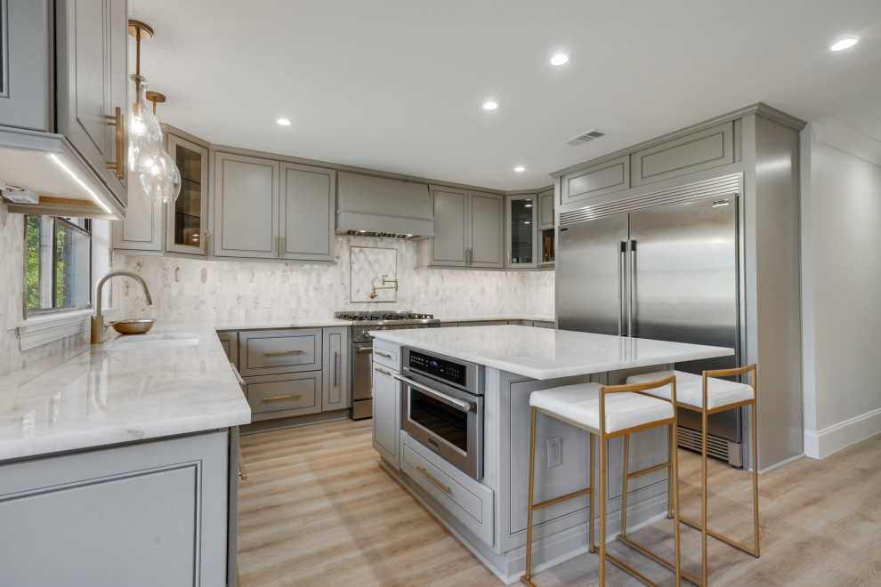 This is an example of a large transitional u-shaped eat-in kitchen in New Orleans with an undermount sink, flat-panel cabinets, grey cabinets, quartzite benchtops, white splashback, marble splashback, stainless steel appliances, light hardwood floors, with island, brown floor and white benchtop.