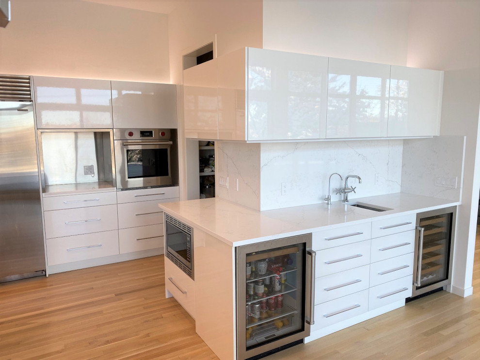 Foto på ett stort funkis vit l-kök, med en undermonterad diskho, släta luckor, vita skåp och vitt stänkskydd