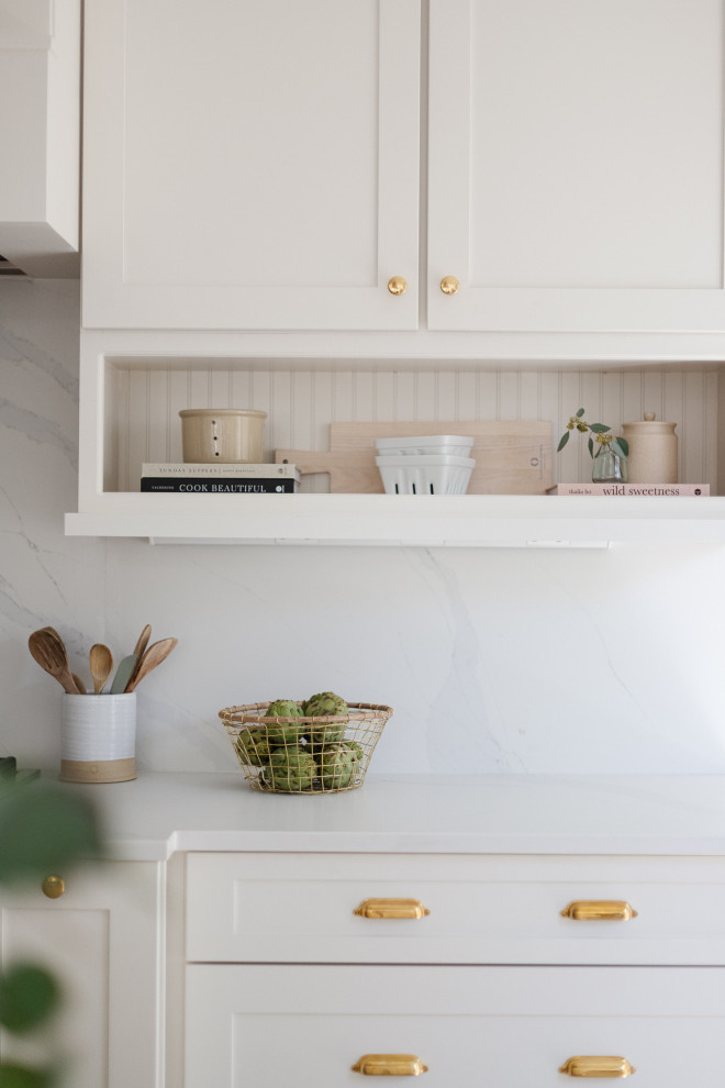 Foto på ett mellanstort vintage vit kök, med en rustik diskho, skåp i shakerstil, vita skåp, bänkskiva i kvarts, vitt stänkskydd, rostfria vitvaror, ljust trägolv, en köksö och brunt golv